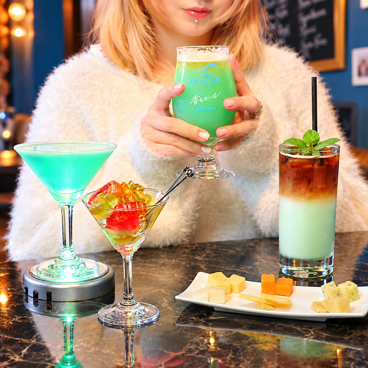 グリーンのビール、エメラルド色のマティーニ、グミを飾ったカクテル、コーヒーとミントのアイスドリンク、チーズの盛り合わせが並ぶバーのテーブル写真